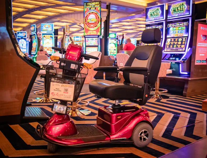 A shiny red mobility scooter with a front basket is parked near slot machines in a well-lit casino.